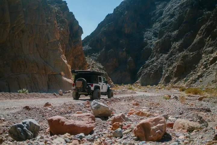 A white Jeep SUV drives through a rugged desert canyon. This versatile vehicle is available for RV rental adventures.. Jeep Wrangler Rubicon 2017