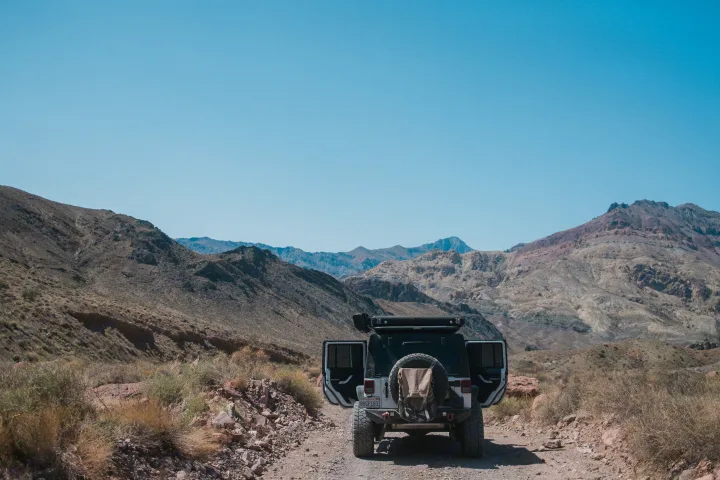 Rear view of a white Jeep on a dusty mountain road, not an RV rental. It's ready for rugged desert adventures amidst tall peaks.. Jeep Wrangler Rubicon 2017