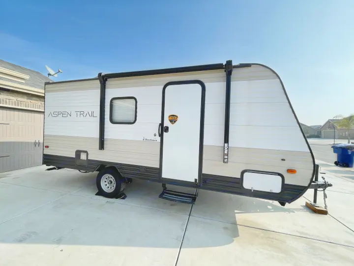 A modern Aspen Trail travel trailer, possibly an RV rental, is parked on a sunny driveway, ready for its next journey.. Aspen Trail LE 2021