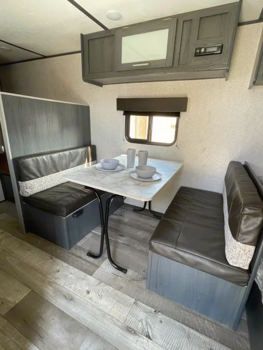 Cozy RV rental dinette featuring a white marble table, dark seating, and sleek overhead storage, perfect for meals on the go.. Aspen Trail LE 2021