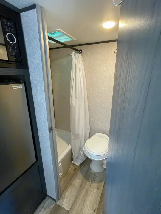 Inside an rv rental: a compact bathroom with shower/tub, toilet, and adjacent microwave/fridge setup.. Aspen Trail LE 2021