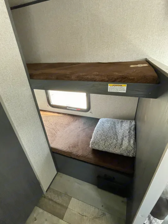RV rental interior featuring cozy bunk beds with brown coverings. The top bunk has a 300 lbs. load capacity warning.. Aspen Trail LE 2021