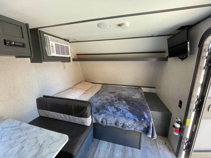 This cozy rv rental showcases a compact bedroom area with a bed, TV, AC, and a small dinette.. Aspen Trail LE 2021