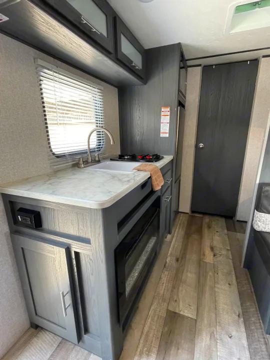 Inside a clean, modern RV rental kitchen featuring a sink, stove, cabinets, and wood-look flooring.. Aspen Trail LE 2021