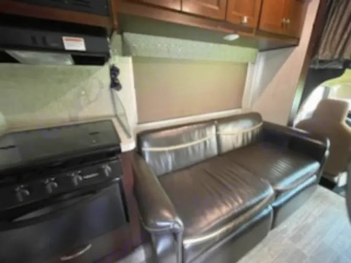 RV rental interior: A compact kitchen with a black stove and microwave, and a comfortable brown sofa by the window.. Forest River Sunseeker 2018