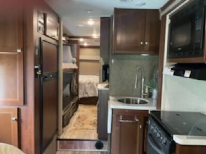 Inside a cozy RV rental: kitchen on right, bunk beds & hallway to a rear bedroom on left. Functional mobile living space.. Forest River Sunseeker 2018
