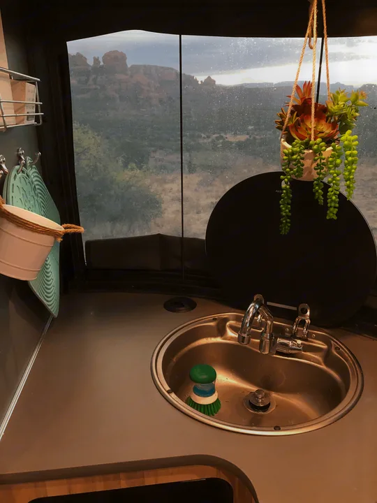 Enjoy the scenic red rock view from your RV rental! This cozy kitchen features a sink, hot pads, and decorative succulents.. Airstream Basecamp X 2021