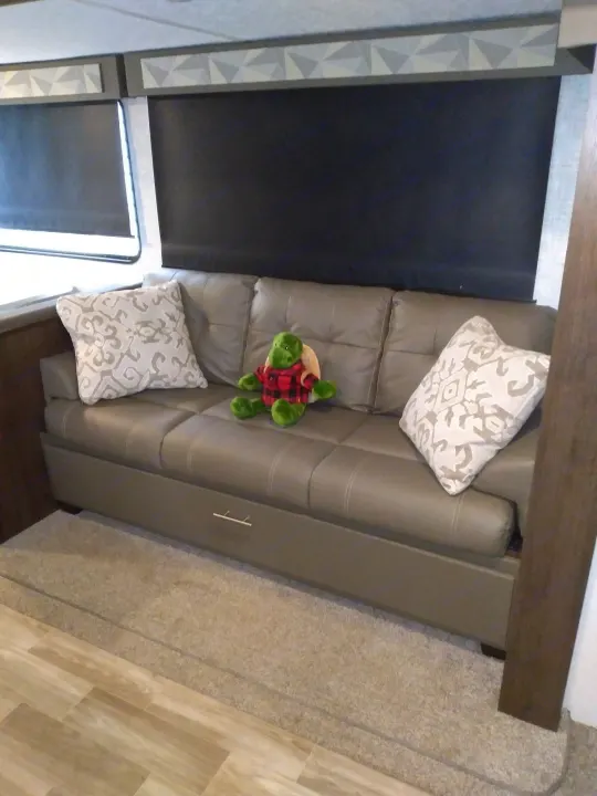 Inside an RV rental: a cozy gray sofa with patterned pillows, a plaid turtle, dark window shades, and mixed flooring.. Forest River Other 2020