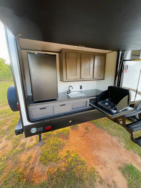 RV rental with an outdoor kitchen setup: black fridge, sink, cabinets, and pull-out two-burner stove.. Cruiser RV MGP 3100BH 2022