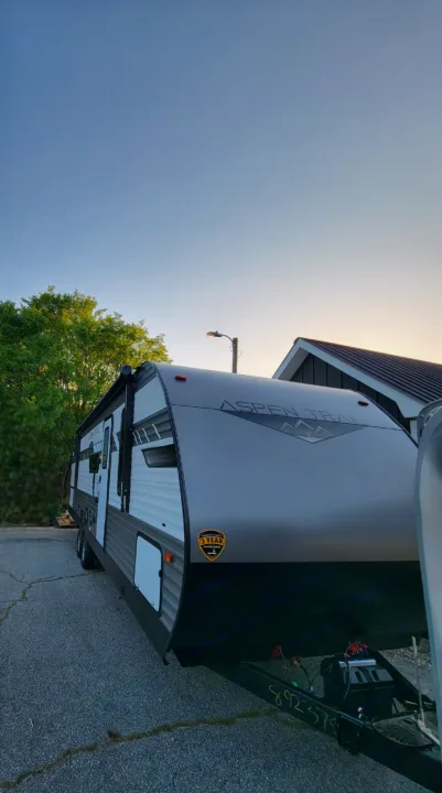 Aspen Trail travel trailer RV, an ideal rv rental option. This sleek, light-colored RV is parked on asphalt, ready for adventure.. Dutchman Aspen Trail 2022