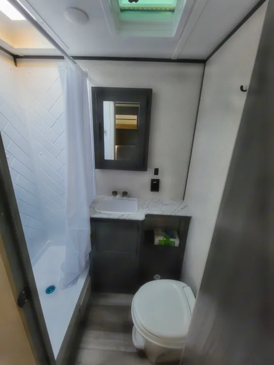 Bright RV rental bathroom with a spacious shower, modern vanity, toilet, and mirrored medicine cabinet.. Dutchman Aspen Trail 2022