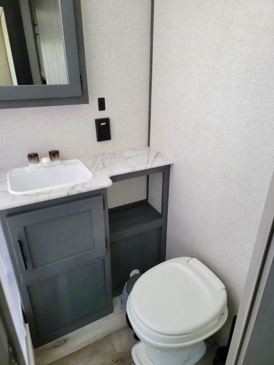 RV rental bathroom: White toilet, gray vanity & sink, plus open storage. Compact, modern interior design.. Dutchman Aspen Trail 2022