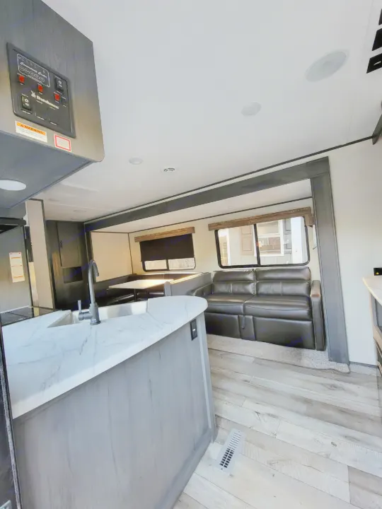 Modern RV rental interior showing kitchen island, comfortable sofa, and dinette area with light wood-look flooring.. Dutchman Aspen Trail 2022