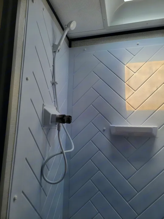 Clean RV rental shower interior with white herringbone walls, shower head, and dual faucets. Sunlight streams in from above.. Dutchman Aspen Trail 2022