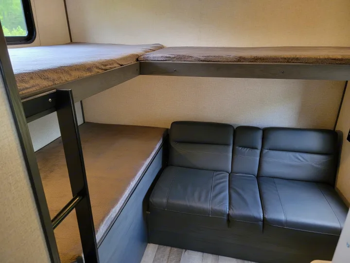 RV rental interior: two cozy bunk beds with gray blankets and a comfortable black sofa for relaxing.. Dutchman Aspen Trail 2022