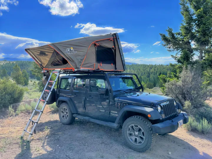 Black Jeep Wrangler with an open Tuff Stuff rooftop tent and ladder, an ideal RV rental for off-grid camping adventures.. Jeep Wrangler Unlimited 2018