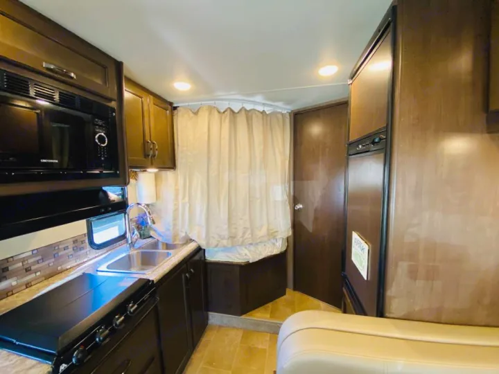 RV rental: Compact kitchen with microwave, stove, sink, and refrigerator. Adjacent is a bathroom with curtained shower.. Thor Chateau 2017