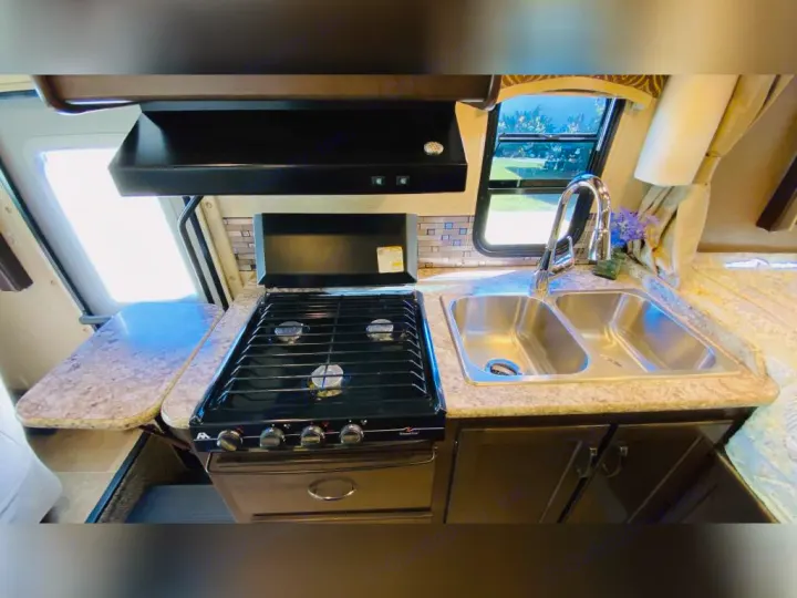 Compact RV rental kitchen features a stove, dual sink, and expandable counter, ideal for road trips.. Thor Chateau 2017