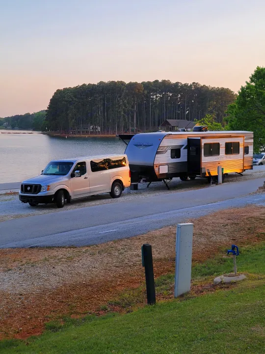 This RV rental travel trailer, hitched to a truck, sits lakeside at a peaceful campground.. Dutchman Aspen Trail 2022