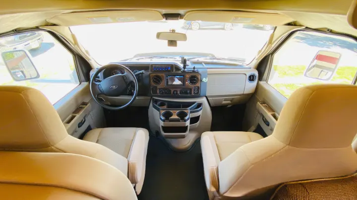 View from inside an RV rental: bright cockpit with steering wheel, dashboard, and two front seats, ready for the road.. Thor Chateau 2017