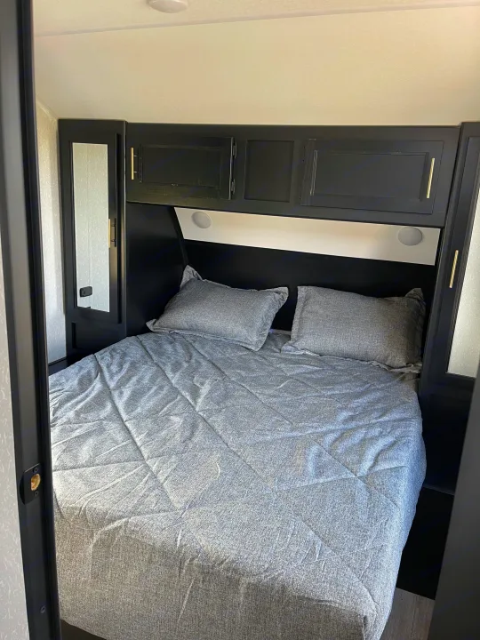 RV rental bedroom: a modern queen bed with integrated lighting, overhead cabinets, and mirrored wardrobes.. Forest River Cherokee Grey Wolf 2022