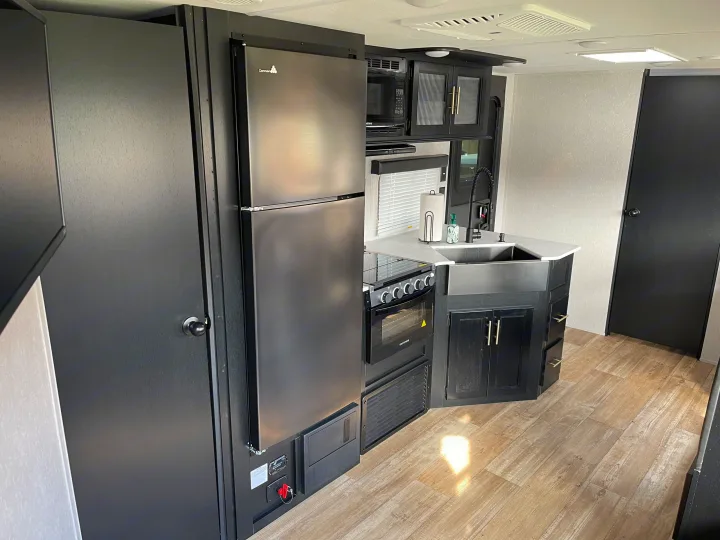 Modern RV rental kitchen featuring a dark stainless steel fridge, oven, sink, and stylish cabinetry, ideal for travel.. Forest River Cherokee Grey Wolf 2022