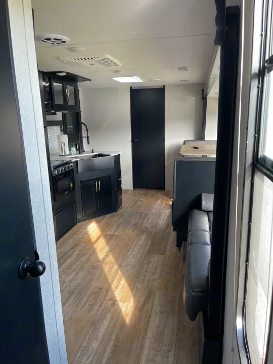 Modern RV rental interior: a full kitchen with black cabinets & appliances, light wood floor, and comfortable living area.. Forest River Cherokee Grey Wolf 2022