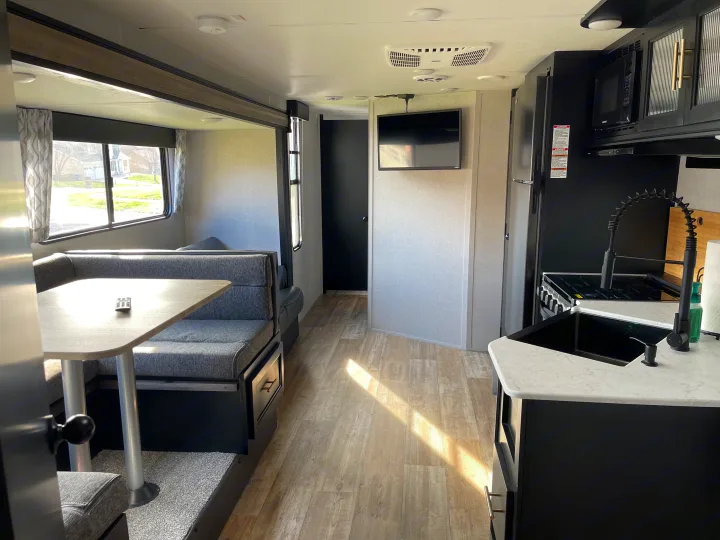 Spacious RV rental interior featuring a modern kitchen, dining booth, TV, and light wood flooring bathed in sunlight.. Forest River Cherokee Grey Wolf 2022