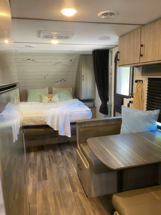 Bright RV rental living space featuring a comfy bed with decorative wall accents, a dining table, and wood-look floors.. Keystone RV Passport SL 2021