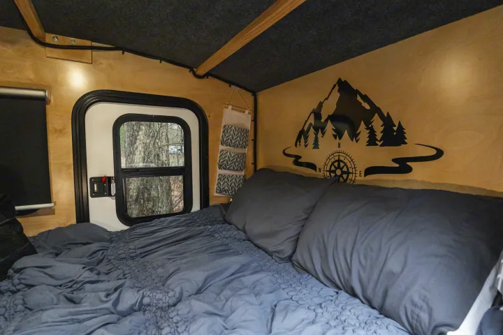 Cozy RV rental interior: comfy bed, window with tree view, and scenic mountain decal, ideal for camping and travel.. Outbound Travel Trailer Extreme 2021