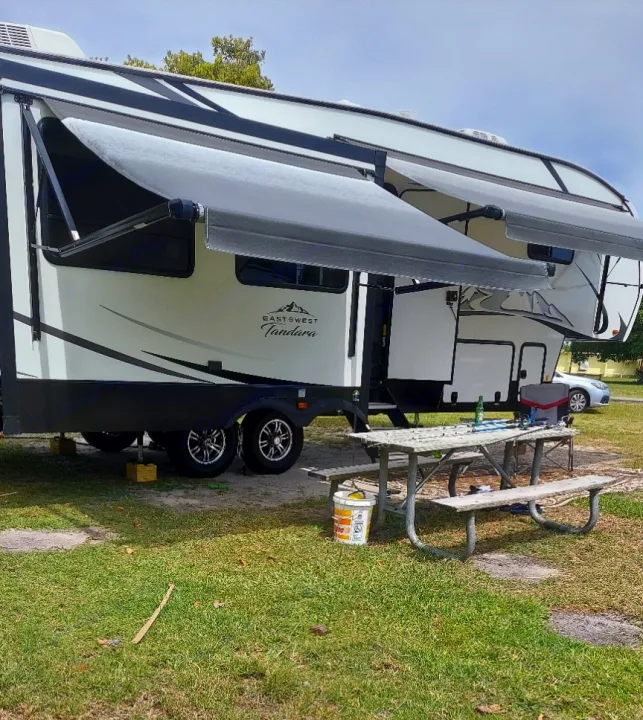 This large white and black East West Tandara RV rental is set up at a grassy campsite, with two extended awnings over a picnic table.. East to West Tandara 2021