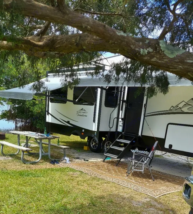This RV rental offers a spacious setup with an extended awning, picnic table, and outdoor rug at a serene campsite.. East to West Tandara 2021