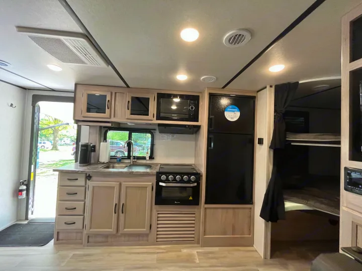 Cozy RV rental kitchen with stove, microwave, fridge, sink, and adjacent bunk beds.. Coachmen 2549 BHX 2021