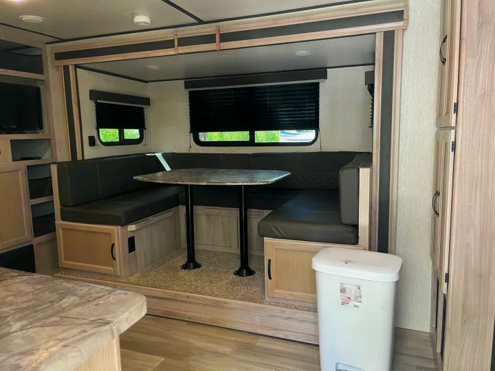 Inside an RV rental: a comfortable U-shaped dinette with black leather cushions, table, and ample storage cabinetry.. Coachmen 2549 BHX 2021
