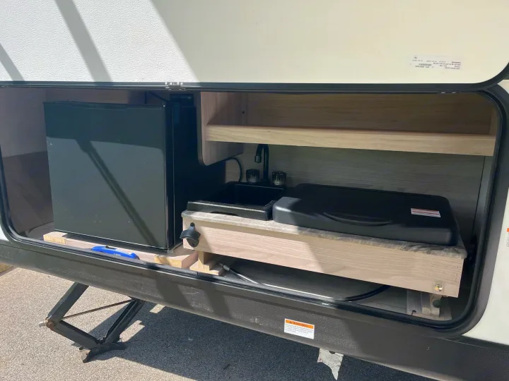 This RV rental features an outdoor kitchen compartment with a mini-fridge, sink, and covered cooktop for easy meal prep.. Coachmen 2549 BHX 2021
