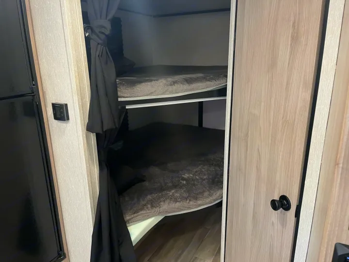 RV rental interior featuring two cozy bunk beds with dark bedding and privacy curtains. A control panel is on the wall.. Coachmen 2549 BHX 2021