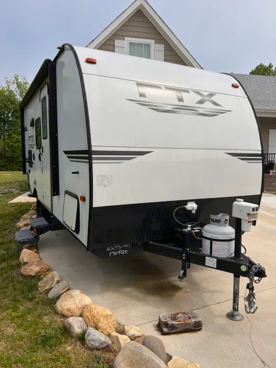 This white travel trailer is parked on a concrete driveway, ready for an RV rental adventure. Visible: propane tank, hitch, steps.. PTX Forest River PDX170 2019