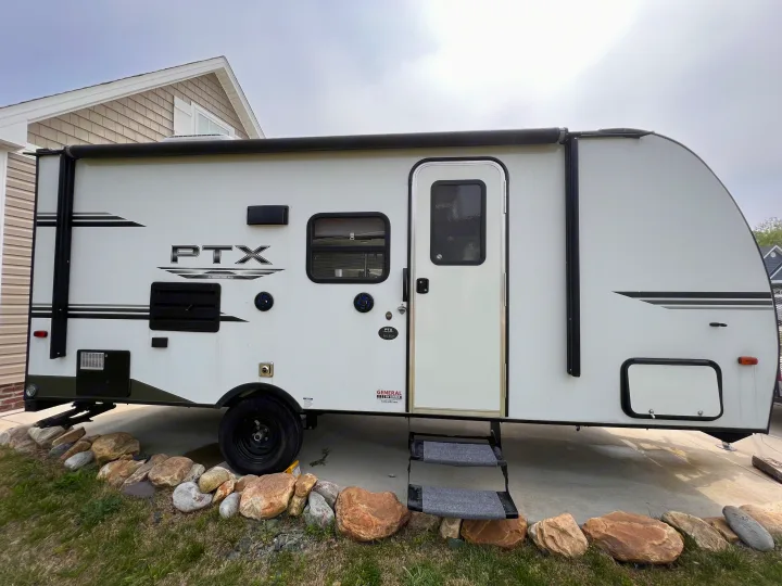 White RV rental travel trailer with an awning, steps, and utility hookups, parked on a concrete pad.. PTX Forest River PDX170 2019