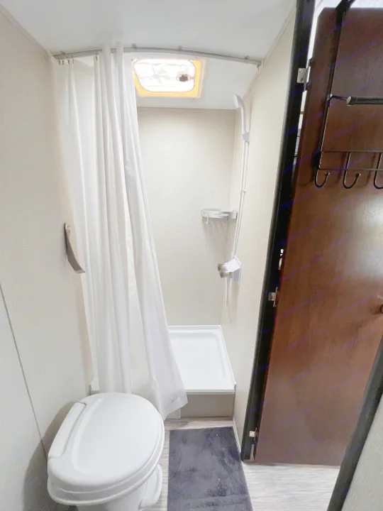 This RV rental bathroom features a white toilet, compact shower with curtain, shower caddy, and a ceiling skylight/vent.. PTX Forest River PDX170 2019