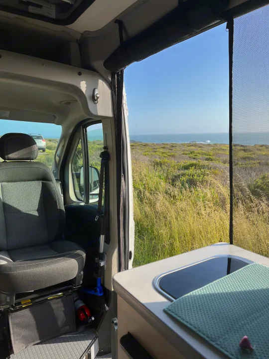Coastal bliss from an rv rental: passenger seat, kitchen, and ocean views through a mesh screen.. Winnebago Solis BUT59P 2024