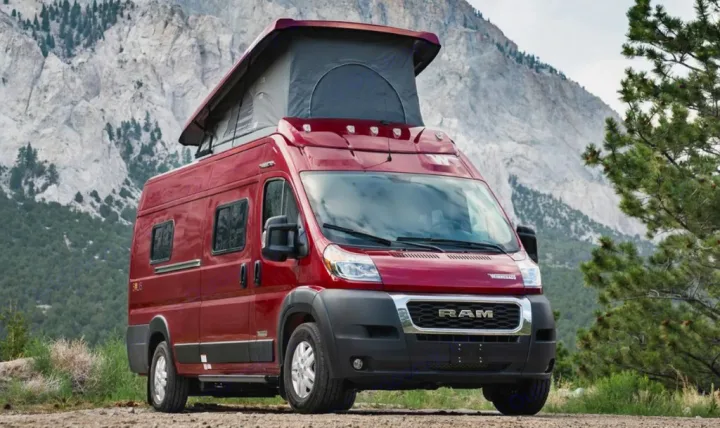 Red pop-top camper van for RV rental, parked on a dirt path with rugged mountains in the background.. Winnebago Solis 2021