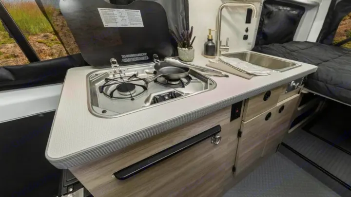 Explore this modern RV rental's compact kitchen with a two-burner stove, sink, and faucet. A comfy bed awaits in the rear.. Winnebago Solis 2021