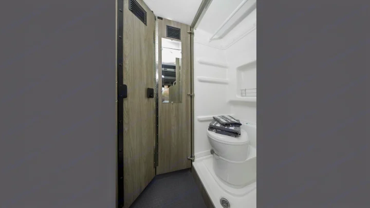 RV rental bathroom with a white toilet, shower area, and a wood-grained door featuring a mirror.. Winnebago Solis 2021