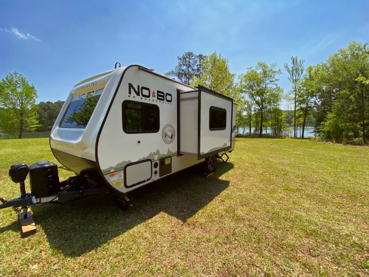 Discover this rv rental: A white No Boundaries camper, slide-out extended, on grass by a lake. Your outdoor adventure begins!. Forest River Other 2022
