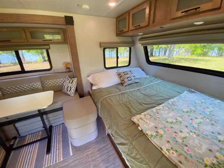 Inviting RV rental interior: a neatly made bed, dinette, and large windows with serene views of trees and water.. Forest River Other 2022