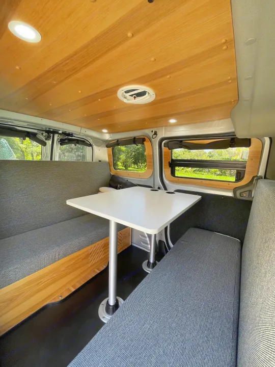 Cozy RV rental interior: a camper van with a wooden ceiling, grey seating, and a white table for dining.. Nissan NV200 2021
