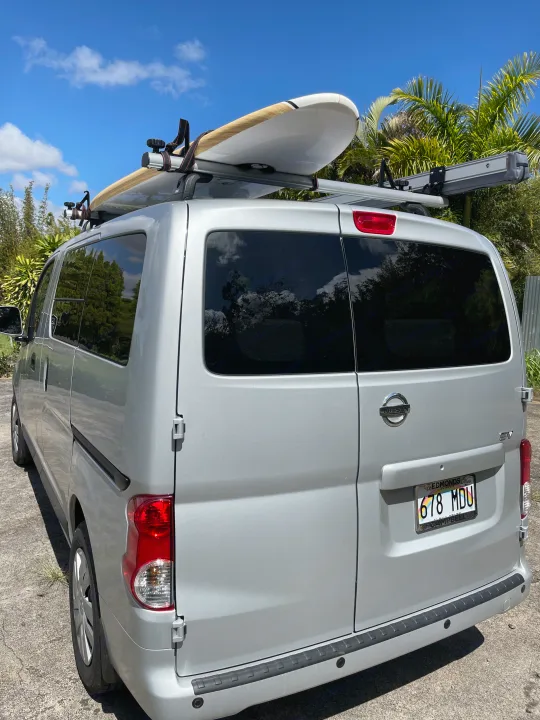 Silver Nissan NV200 van, a versatile RV rental option, with a surfboard ready for beach adventures.. Nissan NV200 2021