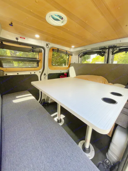 This RV rental's spacious interior features a bright dining table with cup holders, comfy gray benches, and wood-paneled ceiling.. Nissan NV200 2021