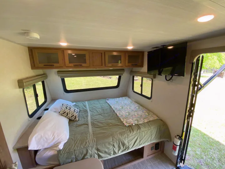 Spacious RV rental bedroom with a comfortable bed, large windows, mounted TV, and ample overhead cabinets.. Forest River Other 2022