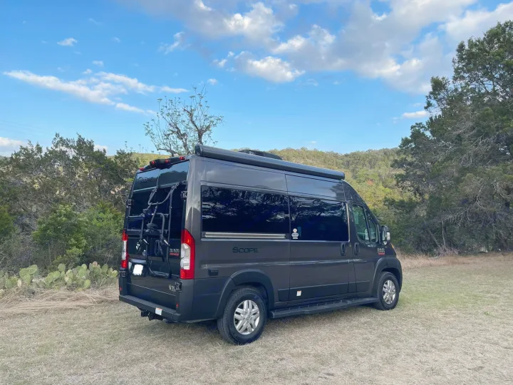Dark grey Scope camper van parked in a grassy field with trees under a blue sky, perfect for your next rv rental adventure.. Thor Scope 18M 2022